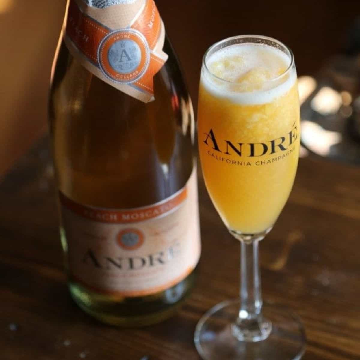 peach moscato cocktail in a champagne glass next to a bottle of moscato