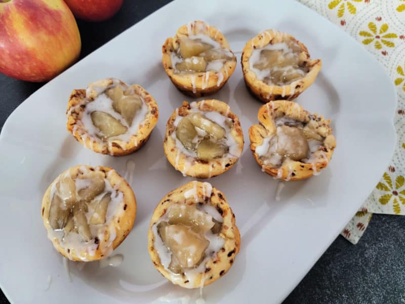 Cinnamon Roll Apple Pie Cups on a white platter with apples in the background