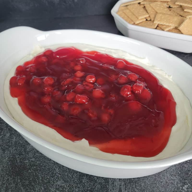 Easy, No-Bake Cherry Cheesecake in a white baking dish next to a bowl of graham crackers