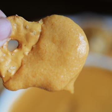 Bagel chip covered in Guinness Beer Cheese Dip above a bowl