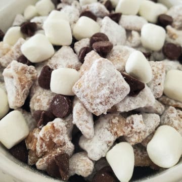 Hot chocolate muddy buddies piled in a white bowl with mini marshmallows and chocolate chips