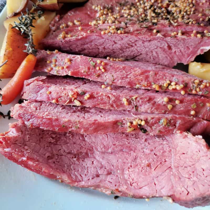Guinness corned beef with seasoning sliced on a white platter with carrots and potatoes