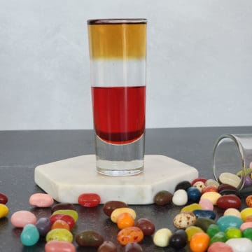 Layered jelly bean shot on a white coaster surrounded by jelly beans