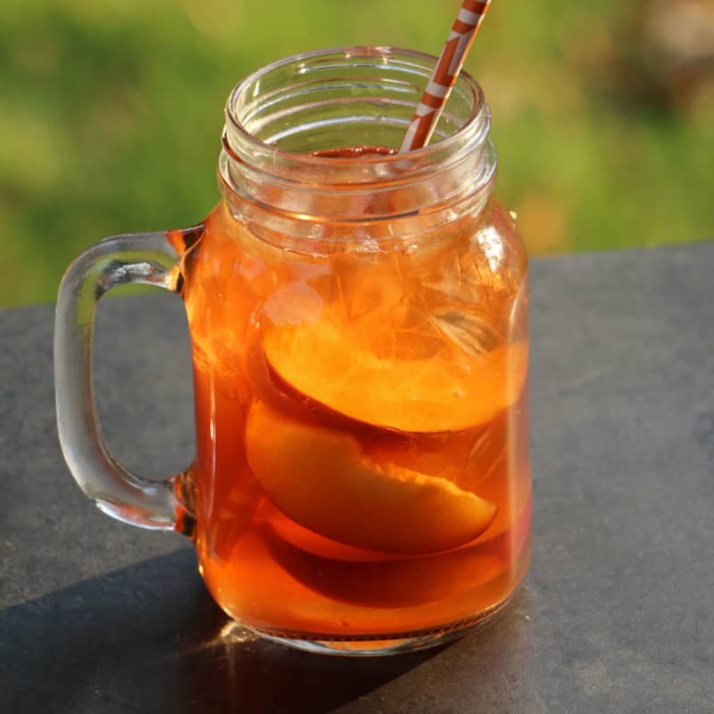 Peach Iced Tea Cocktail in a mason jar glass with sliced peaches and a paper straw