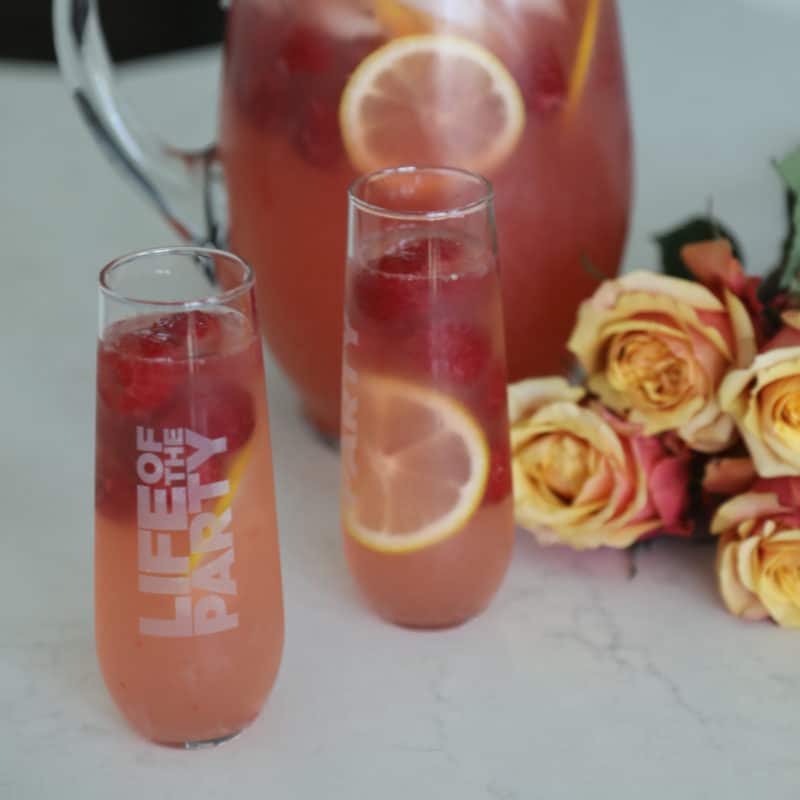 Raspberry Lemonade Moscato Punch in two glasses and a large pitcher next to roses