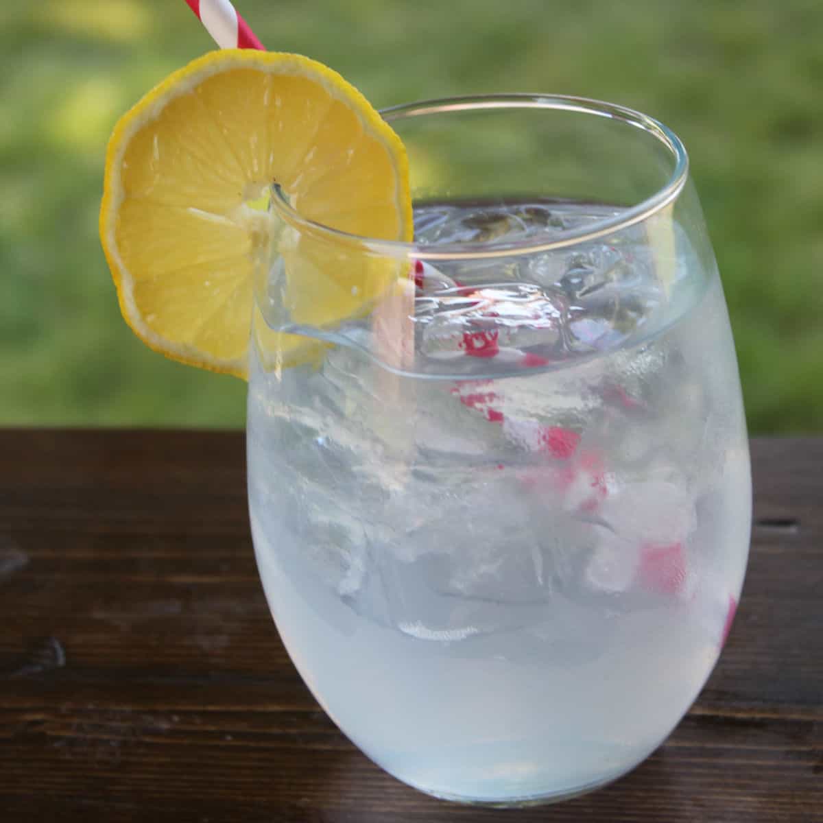 Raspberry Pomegranate Lemonade Cocktail in a glass with a lemon wheel and paper straw