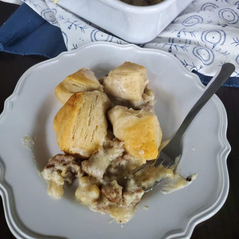 Sausage biscuit and gravy casserole serving on a white plate near the baking dish