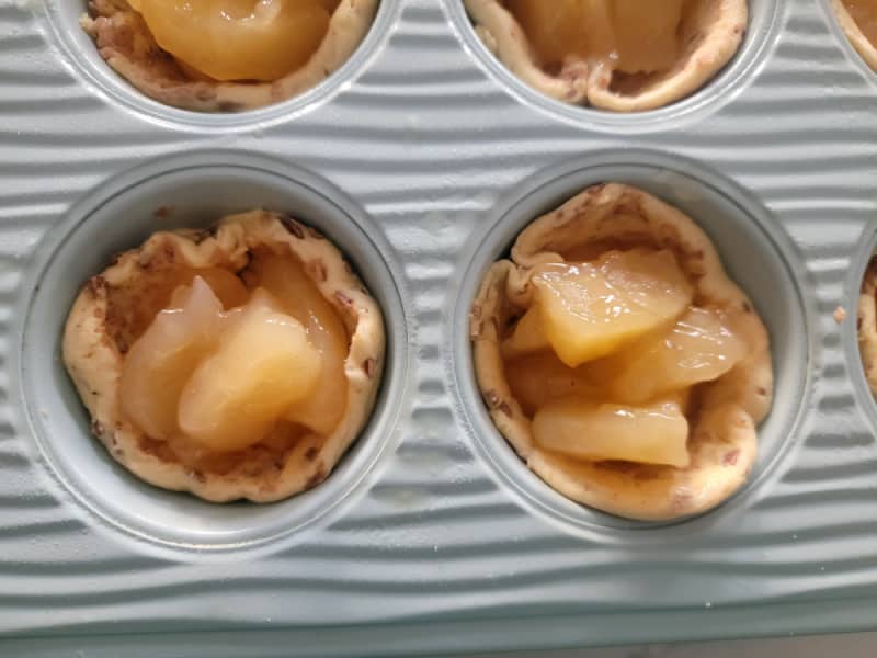 Unbaked Cinnamon Roll Apple Pie cups in a blue muffin tin