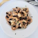 air fried mushrooms in a white bowl next to a wooden spoon and napkin