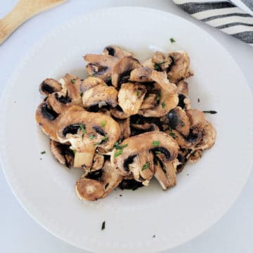 air fried mushrooms in a white bowl next to a wooden spoon and napkin