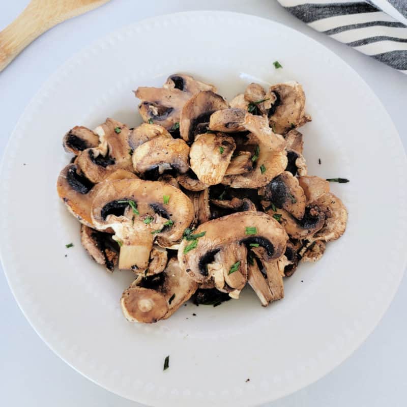 air fried mushrooms in a white bowl next to a wooden spoon and napkin