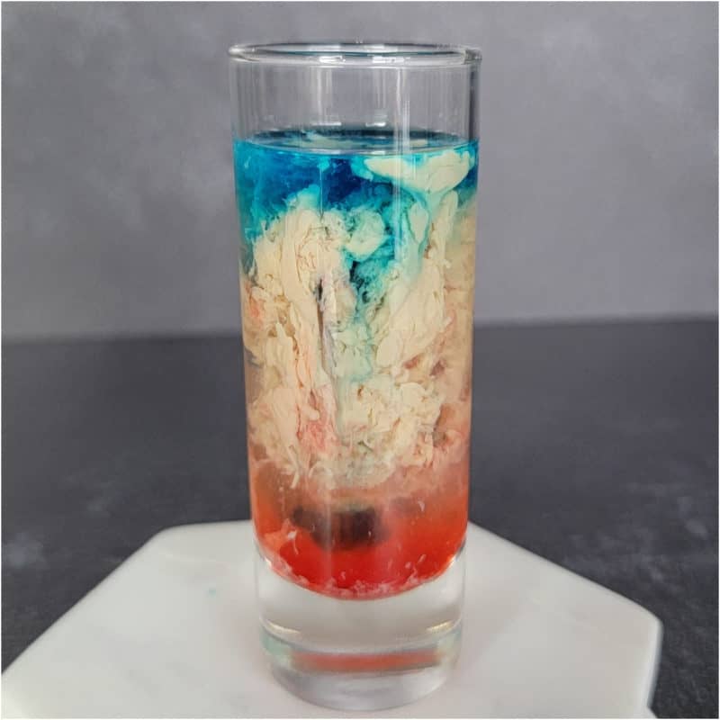 Blue Cream and Red alien brain hemorrhage shot in a clear glass on a white coaster.