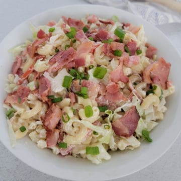 BLT pasta salad garnished with green onion in a white bowl
