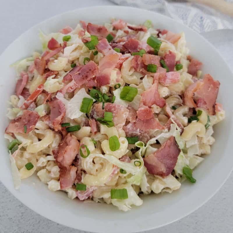 BLT pasta salad garnished with green onion in a white bowl