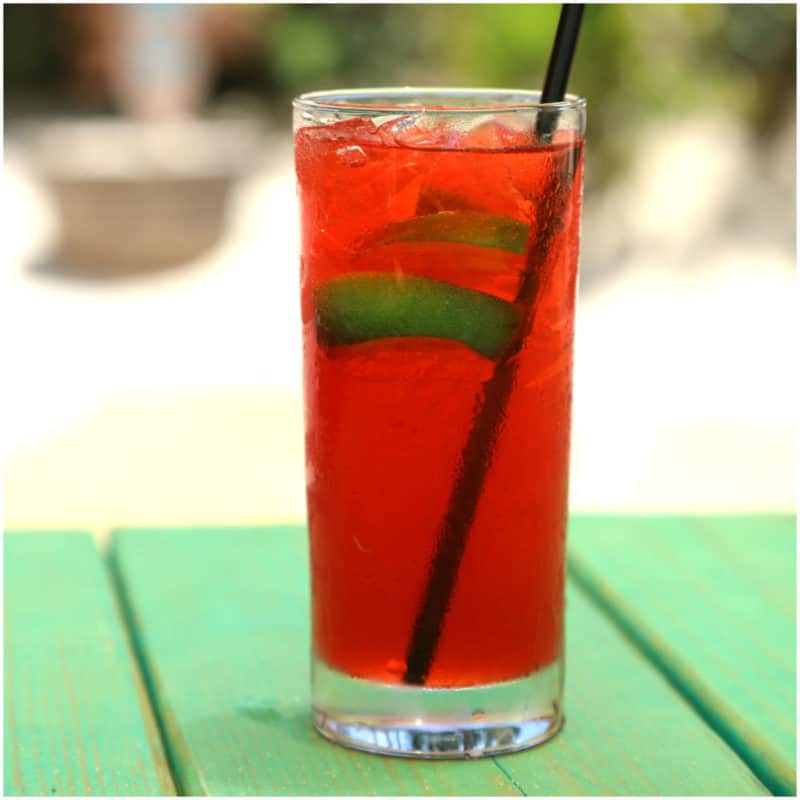 Red cocktail with lime slices in a tall glass on a green picnic table