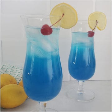 Blue Lagoon Cocktail in Hurricane glasses with lemon wheel and cherry
