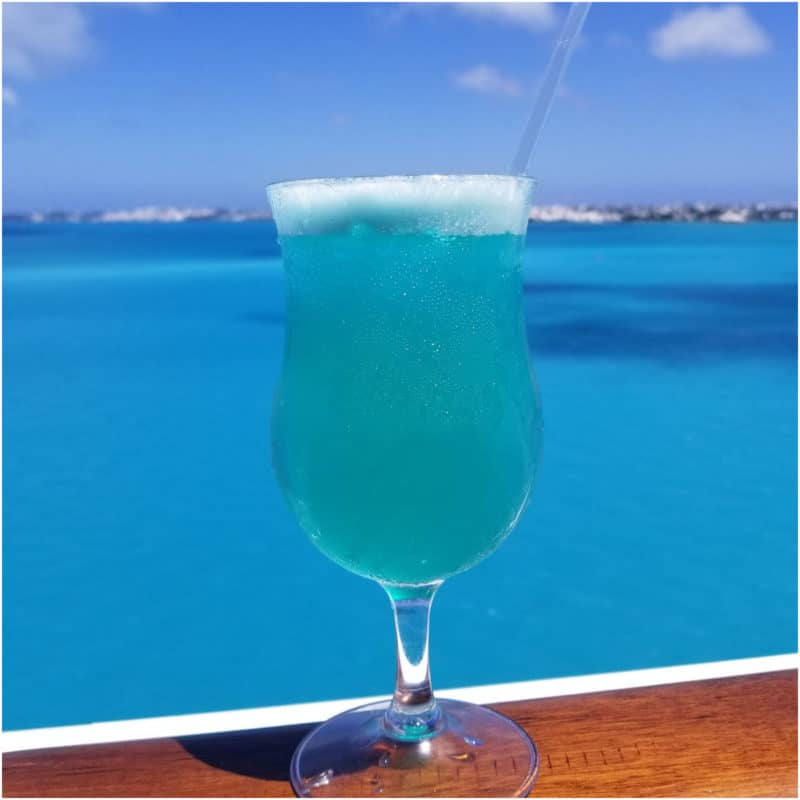 Blue Margarita on a wood rail with the ocean behind it