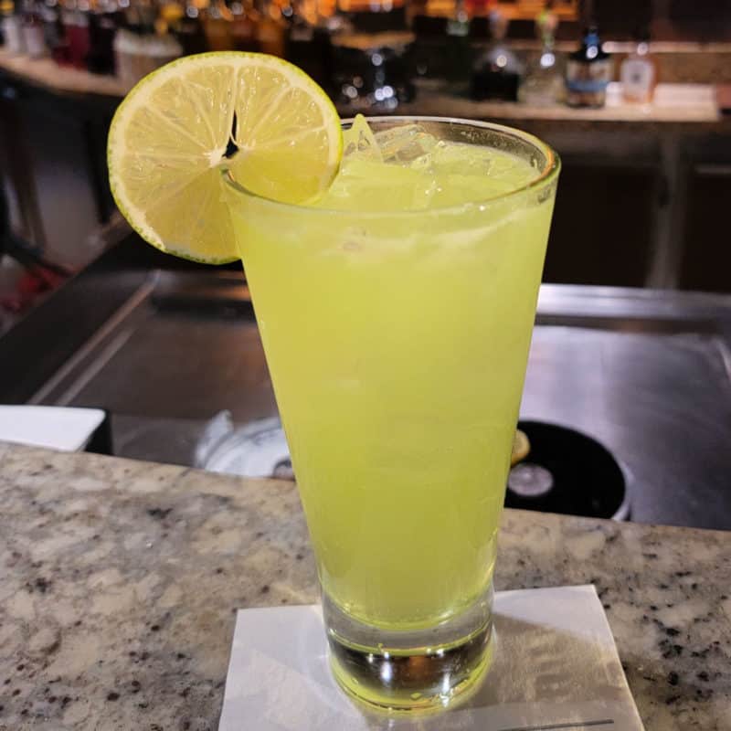 yellow green cocktail in a tall glass with lime circle