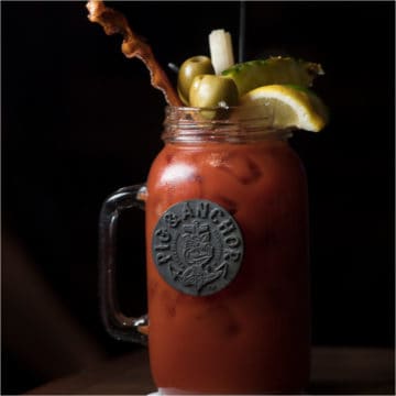 bloody mary cocktail in a large mason jar glass garnished with bacon, olives, and lemon