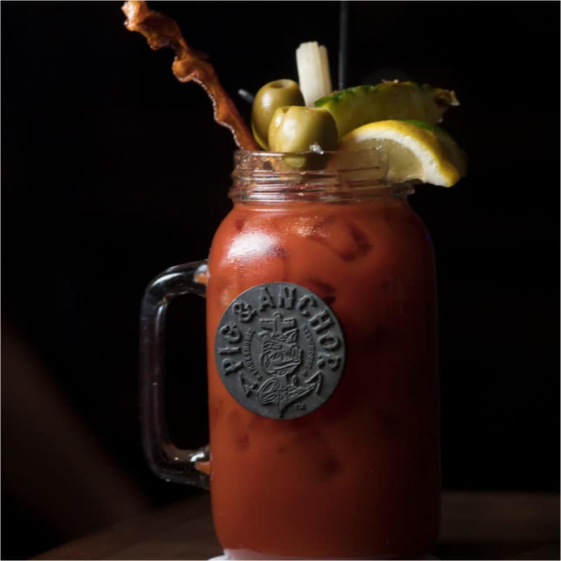 bloody mary cocktail in a large mason jar glass garnished with bacon, olives, and lemon