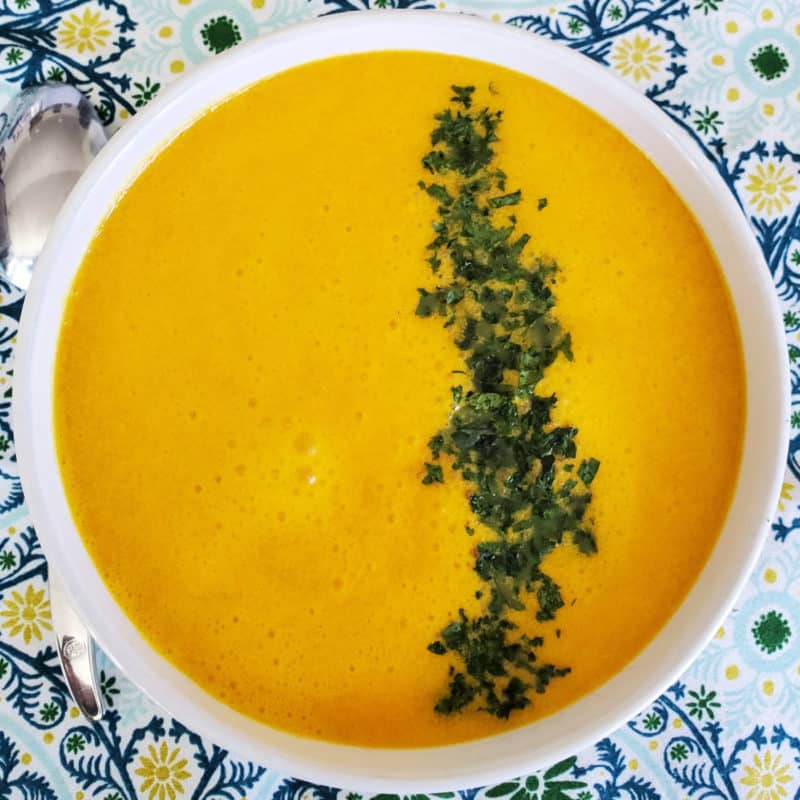Carrot ginger soup with green garnish in a line in a white bowl