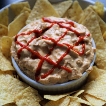 Sriracha garnish on sriracha chicken dip in a white bowl surrounded by tortilla chips