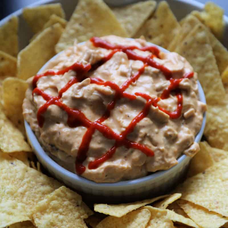 Sriracha garnish on sriracha chicken dip in a white bowl surrounded by tortilla chips 