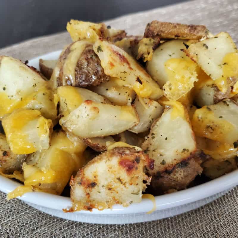 cheese covered potato chunks in a white bowl