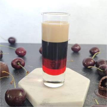 Layered red, brown, and cream shot surrounded by chocolate covered cherries