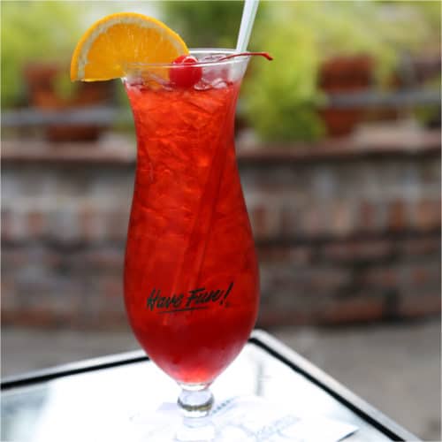 Red cocktail in a Hurricane Glass garnished with an orange wedge