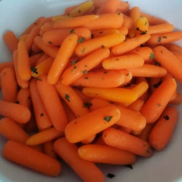 Carrots garnished with greens in a white bowl
