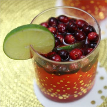 Cranberries and lime in a red cocktail in a glass with gold polka dots