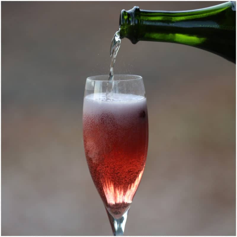green champagne bottle pouring into a champagne flute with cranberry mimosa