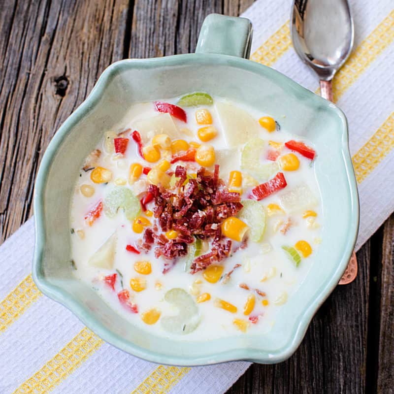 Bacon and corn chowder in a ceramic bowl next to a spoon on a cloth napkin