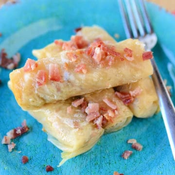 Cabbage rolls garnished with bacon on a blue plate next to a silver fork