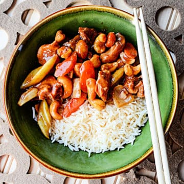 cashew chicken next to white rice in a green bowl with chopsticks