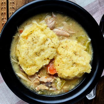 Crockpot chicken and dumplings in a dark bowl next to a spoon