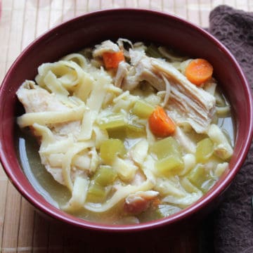 Crockpot chicken noodle soup with noodles, chicken, carrots, and celery in a red bowl