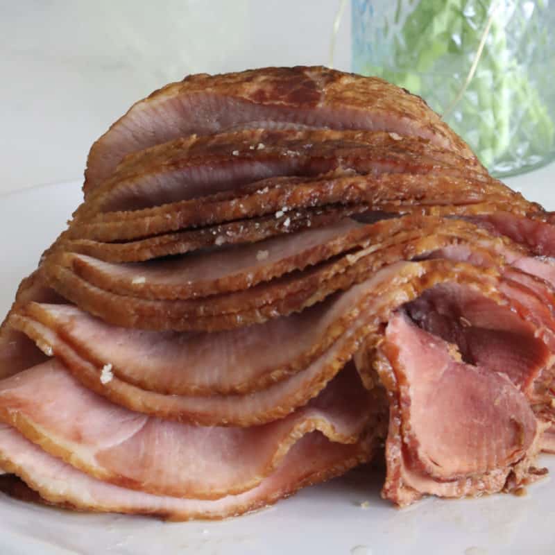 Close up of spiral ham next to a vase on a white platter