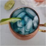 Blue mule in a copper mug with a lime wedge and limes nearby