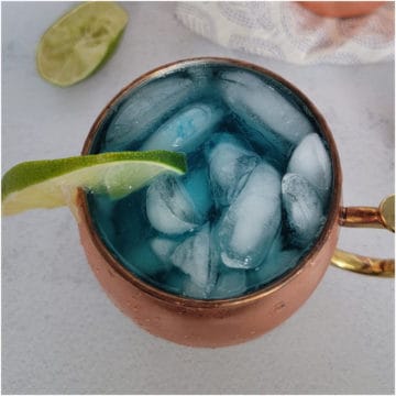 Blue mule in a copper mug with a lime wedge and limes nearby