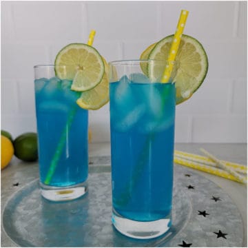Blue electric lemonade in a tall glasses with lemon and lime wheels and yellow paper straw