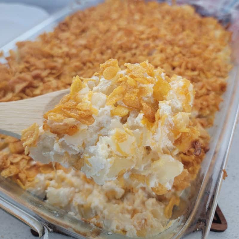 Funeral potatoes on a spoon above a casserole dish