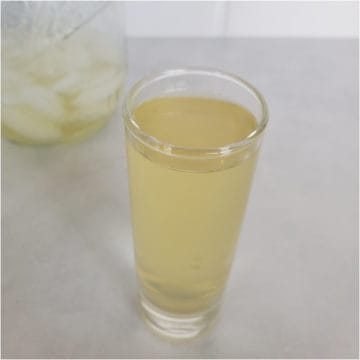 Green tea shot in a clear shot glass next to a mason jar