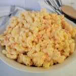 Hawaiian Mac Salad in a white bowl next to plates and a wooden spoon