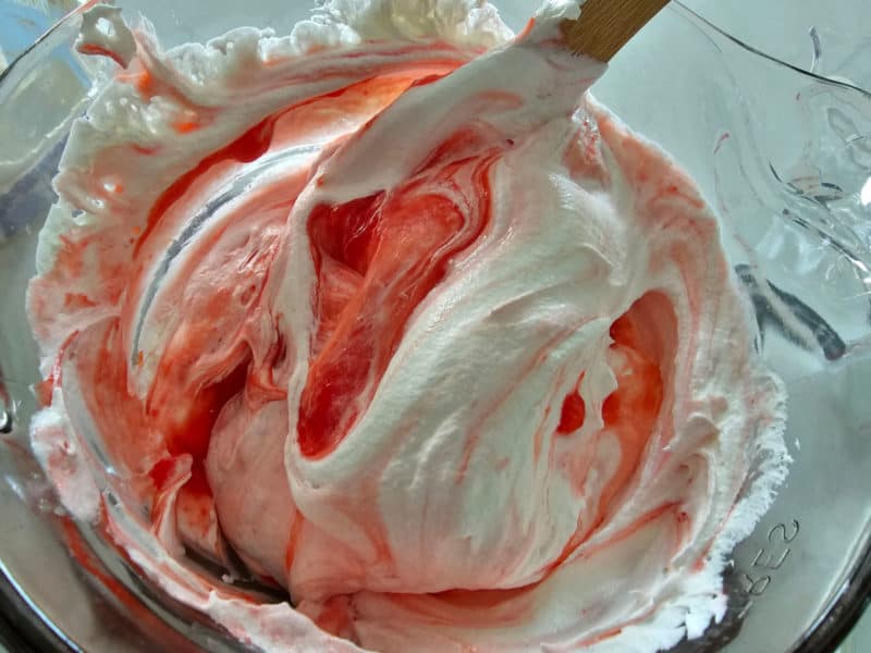 Cool Whip mixing into strawberry fluff with a wooden spoon in a glass bowl