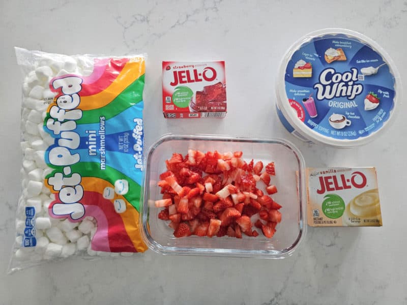 Jet Puff mini marshmallows, Strawberry Jello box, Cool Whip, Diced Strawberries, and Vanilla pudding box for Strawberry Fluff Salad on a white counter