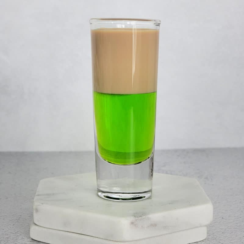 Layered brown and green cocktail shot on two white coasters