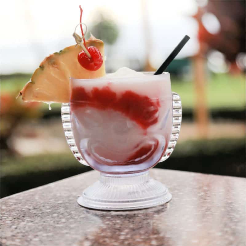 red and white lava flow cocktail in a tiki glass with pineapple wedge and cherry garnish