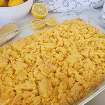 Lemon dump cake in a glass casserole dish with a bowl of lemons in the background